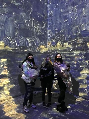 Three students standing in front of projection of Starry Night Over The Rhone by Van Gogh