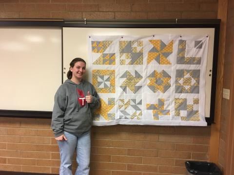 student standing next to quilt top they made